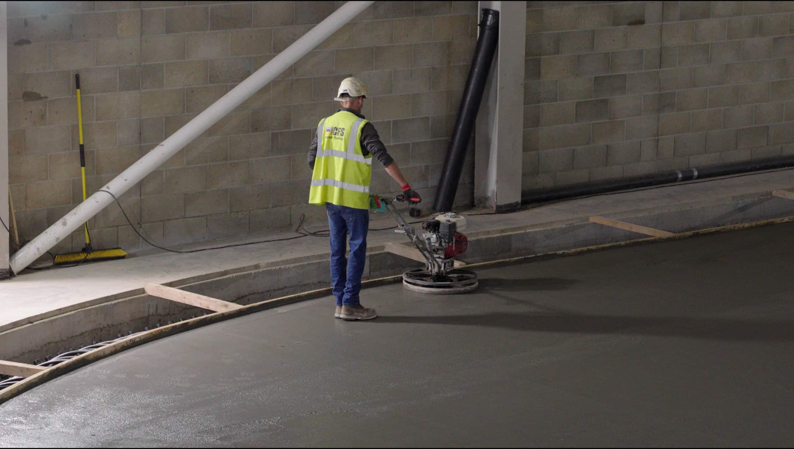 A worker levelling a concrete floor with a high vis vest and hard hat