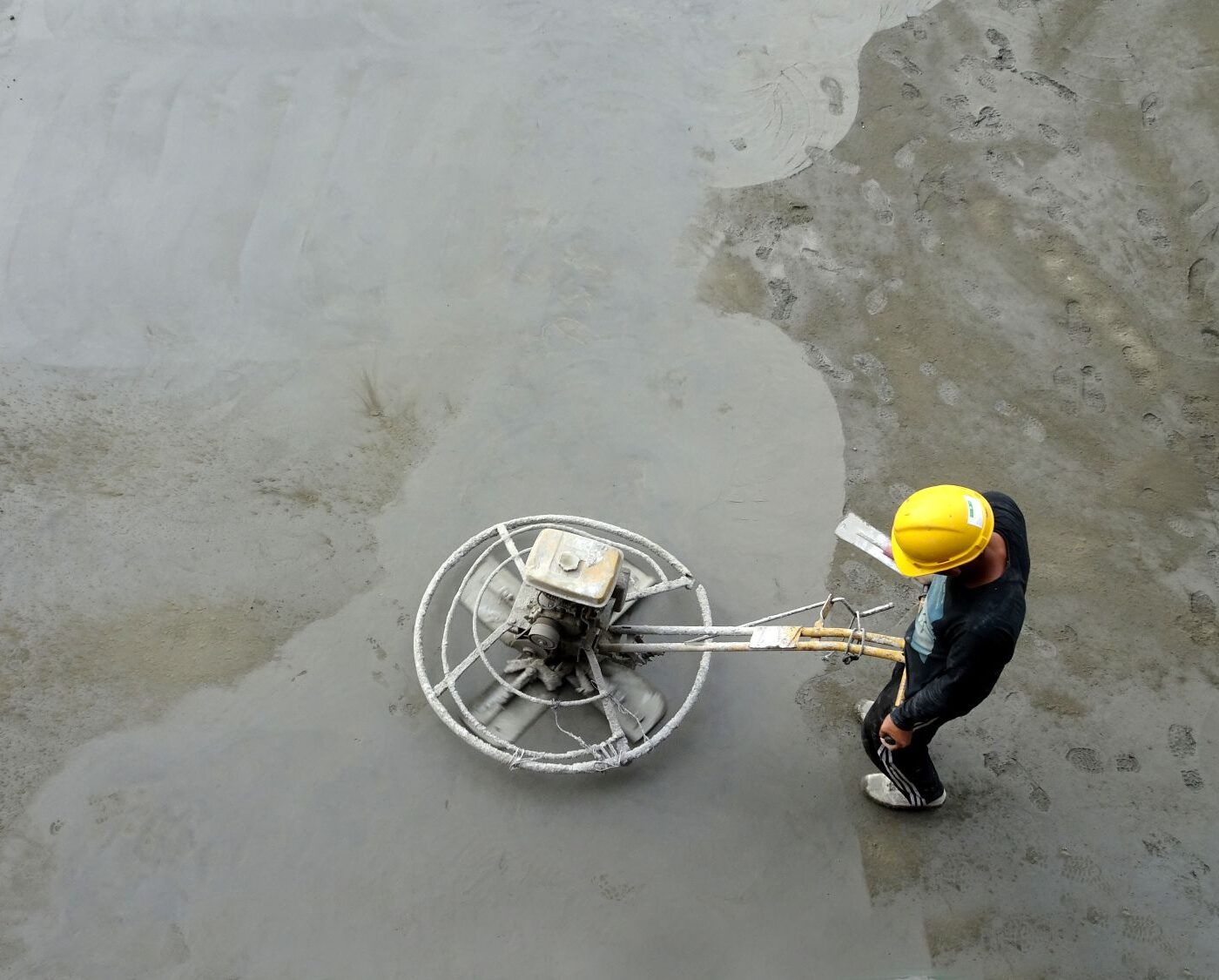 workman using power float on concrete floor.